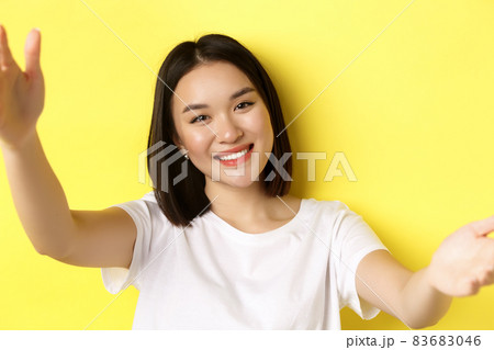 Close up of modern asian girl taking selfie on smartphone, mobile camera view of pretty woman smiling, standing over yellow background Close up of modern asian girl taking selfie on smartphone, mobile camera view of pretty woman smiling, standing over yellow background 83683046
