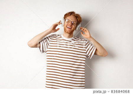 Technology concept. Happy redhead man listening music in headphones and singing along, standing over white background 83684068