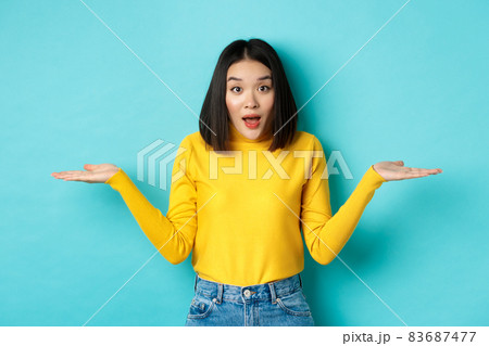 Image of indecisive asian woman shrugging shoulders, spread hands sideways and looking clueless at camera, standing confused against blue background Image of indecisive asian woman shrugging shoulders, spread hands sideways and looking clueless at camera, standing confused against blue background 83687477