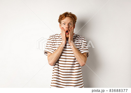 Impressed young man with ginger hair, gasping and staring shocked at camera, express complete disbelief and amazement, white background Impressed young man with ginger hair, gasping and staring shocked at camera, express complete disbelief and amazement, white background 83688377