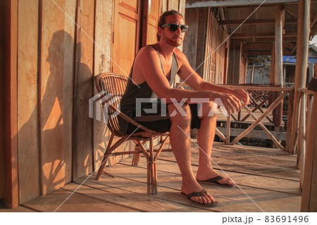 A man sitting on a rattan chair and relaxing on the balcony during the sunset A man sitting on a rattan chair and relaxing on the balcony during the sunset 83691496