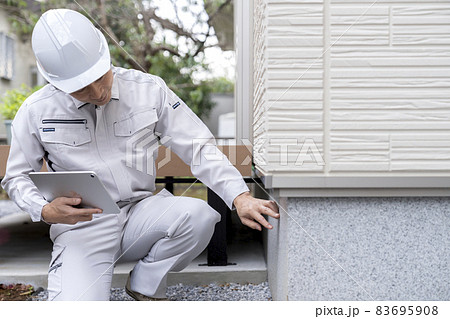 住宅の基礎部分を点検する作業服の男性 83695908