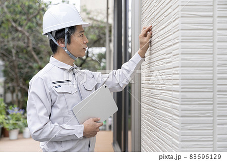 タブレットを持って外壁の検査をする作業服姿の男性 83696129