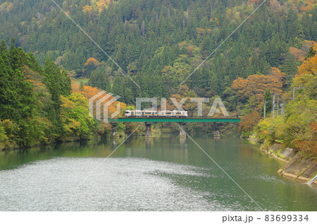 秋のダム湖を通過するローカル列車 83699334