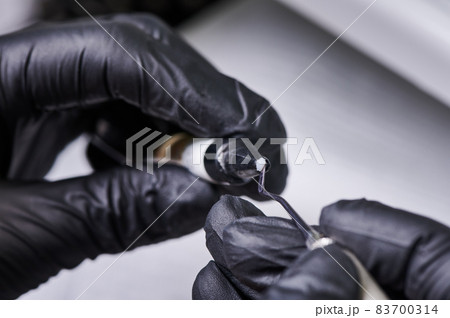 Close up of doctor hands in black sterile gloves preparing bracket bonding paste. Specialist holding dental instrument and adhesive paste for braces placement. Concept of orthodontic treatment 83700314