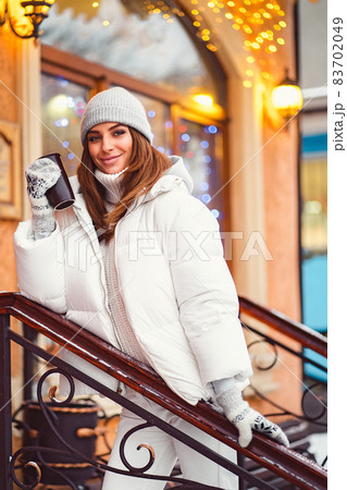 Smiling girl stands on stairs outside while holds coffe to go in hand. Festive mood. Christmas time Smiling girl stands on stairs outside while holds coffe to go in hand. Festive mood. Christmas time 83702049