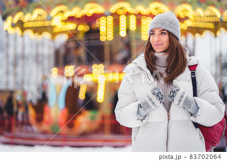 Positive girl in white coat walks at the Christmas city while holds backpack. Lifestyle, Holidays  83702064
