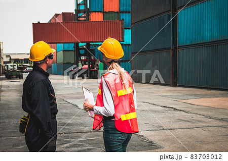 Industrial worker works with co-worker at overseas shipping container yard Industrial worker works with co-worker at overseas shipping container yard 83703012
