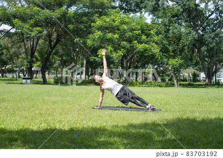Sporty active young man in sportswear doing sport exercises in the park. Fit caucasian man doing side plank exercise on the black sports mat outdoors. Sporty active young man in sportswear doing sport exercises in the park. Fit caucasian man doing side plank exercise on the black sports mat outdoors. 83703192