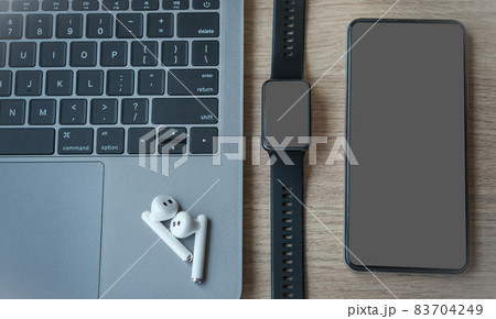 Close-up of Keyboard laptop computer, wireless earphones focus with smartwatch and smartphone empty screen on wooden background office desk in coffee shop like the background 83704249