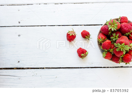 Ripe red strawberries lie in a white cup on a wooden white table. Copy space. View from above. Ripe red strawberries lie in a white cup on a wooden white table. Copy space. View from above. 83705392