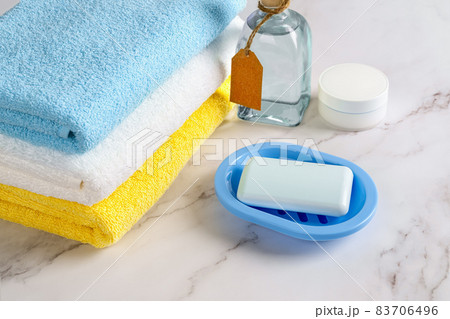 Soap on a blue dish, skin moisturizer and tonic lotion near stack of colored cotton terry towels Soap on a blue dish, skin moisturizer and tonic lotion near stack of colored cotton terry towels 83706496