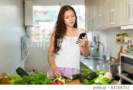 Woman using phone while making vegetable salad Woman using phone while making vegetable salad 83708752