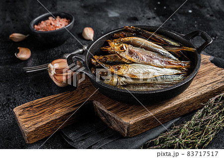 Hot Smoked sprat and Anchovy fishes in pan. Black background. Top view 83717517