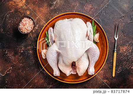 Chicken, raw poultry in a rustic plate with rosemary. Dark background. Top view Chicken, raw poultry in a rustic plate with rosemary. Dark background. Top view 83717874