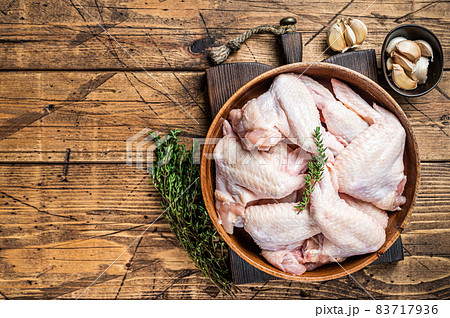 Raw chicken wings in a wooden plate with thyme and garlic. Wooden background. Top view. Copy space Raw chicken wings in a wooden plate with thyme and garlic. Wooden background. Top view. Copy space 83717936