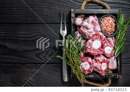 Raw veal beef Oxtail Meat in wooden tray with thyme. Black wooden background. Top view. Copy space 83718323
