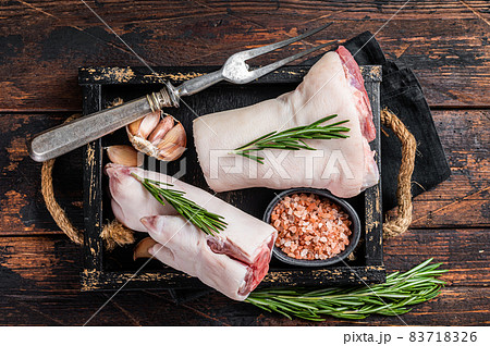 Uncooked Raw pork hoof, knuckle, feet in a wooden tray with herbs. Wooden background. Top view Uncooked Raw pork hoof, knuckle, feet in a wooden tray with herbs. Wooden background. Top view 83718326