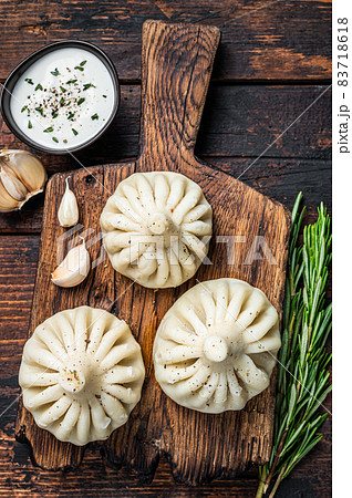 Georgian Khinkali Dumplings with beef and lamb meat on wooden board with herbs. Dark wooden background. Top view Georgian Khinkali Dumplings with beef and lamb meat on wooden board with herbs. Dark wooden background. Top view 83718618