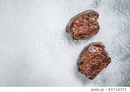 Grilled fillet mignon or tenderloin beef steak on kitchen table. White background. Top view. Copy space Grilled fillet mignon or tenderloin beef steak on kitchen table. White background. Top view. Copy space 83718755
