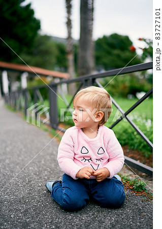 Little girl sitting near a metal fence in a green park Little girl sitting near a metal fence in a green park 83727101