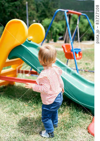 Little girl stands near the children slide in the playground Little girl stands near the children slide in the playground 83727108