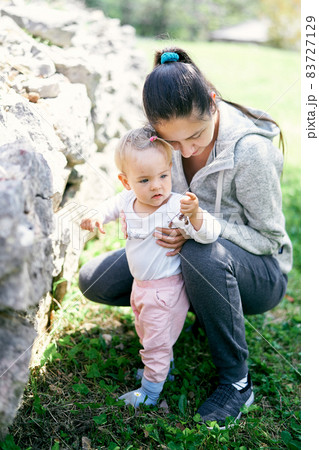 Mom sat down next to her and hugged a little girl near the stones in a green park Mom sat down next to her and hugged a little girl near the stones in a green park 83727129