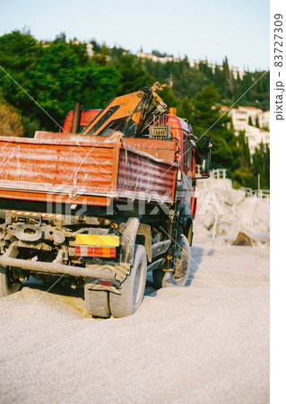 Red car with a forklift stands on the sand against a background of green trees. Back view Red car with a forklift stands on the sand against a background of green trees. Back view 83727309