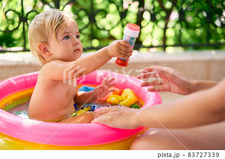 Cute wet baby sits in a small inflatable pool with toys Cute wet baby sits in a small inflatable pool with toys 83727339