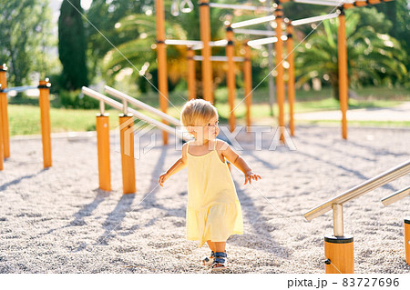 Little girl walks along the playground past the horizontal bars Little girl walks along the playground past the horizontal bars 83727696