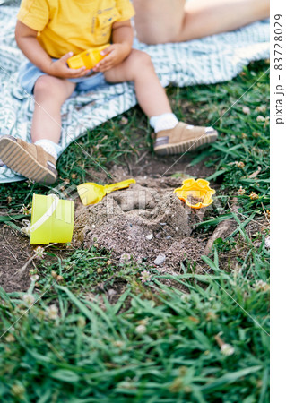Legs of a toddler sitting on a blanket on a green lawn next to toys Legs of a toddler sitting on a blanket on a green lawn next to toys 83728029