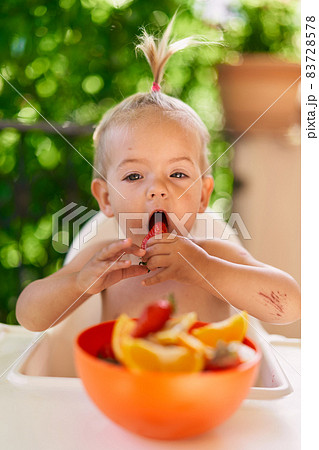 Little girl bites strawberry while holding it by her hands Little girl bites strawberry while holding it by her hands 83728578
