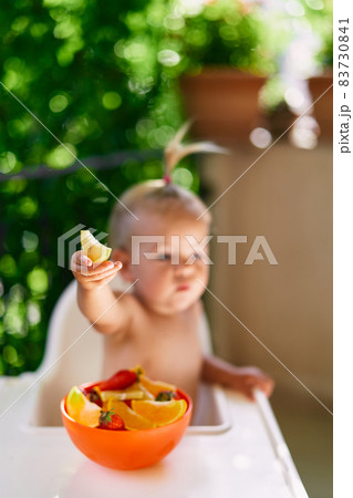 Little girl sits on a high chair on the balcony and holds a slice of orange 83730841