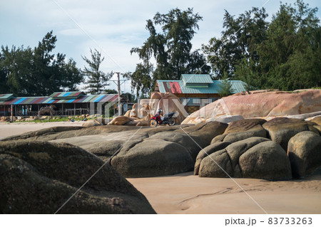 Motorcycle stands on a large stone on the beach. Beach in Asia with large rocks and colorful houses. High quality photo 83733263
