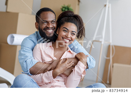 Satisfied young african american husband and wife, hugging, take a break from moving to new apartment among boxes 83734914
