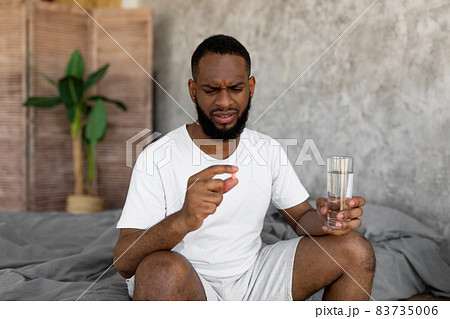 Black man taking pills holding glass of water Black man taking pills holding glass of water 83735006