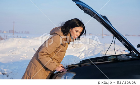 Lady looks at engine of broken automobile on snowy road Lady looks at engine of broken automobile on snowy road 83735656