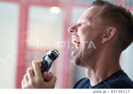Young happy man singing into electric razor Young happy man singing into electric razor 83736117