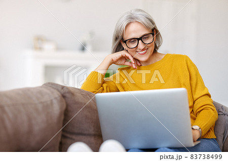 Portrait of happy smiling senior woman resting relaxing on sofa with laptop at home Portrait of happy smiling senior woman resting relaxing on sofa with laptop at home 83738499