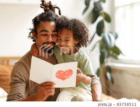Cute african american little boy son giving his father handmade greeting postcard on Fathers Day Cute african american little boy son giving his father handmade greeting postcard on Fathers Day 83738511