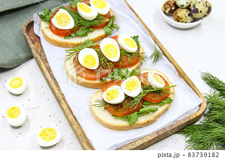 Fresh toast sandwiches with quail eggs, tomatoes and green herbs. Closeup. Top view. Copy space. 83739182