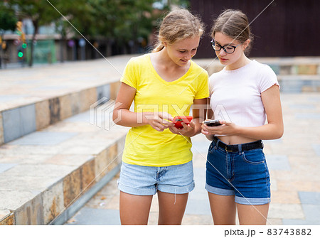 Two young girls with smartphones standing in park 83743882