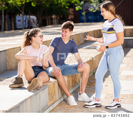 Teenagers using phones and chatting on streets in summer Teenagers using phones and chatting on streets in summer 83743892