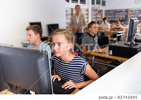 Schoolgirl using computer at lesson, teacher teaching pupils Schoolgirl using computer at lesson, teacher teaching pupils 83743895
