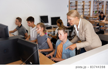 Schoolchildren using computers and teacher teaching them 83744398