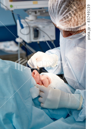 Close up of the face of a patient who is undergoing blepharoplasty. The surgeon cuts the eyelid and performs manipulations using medical instruments Close up of the face of a patient who is undergoing blepharoplasty. The surgeon cuts the eyelid and performs manipulations using medical instruments 83749139
