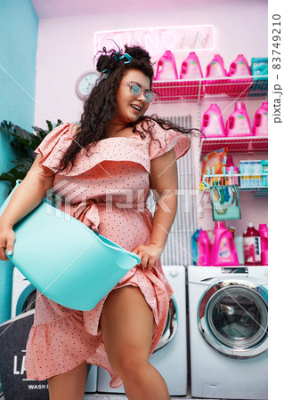 Young stylish plus size woman holding laundry basket smiling friendly in the laundry Young stylish plus size woman holding laundry basket smiling friendly in the laundry 83749210