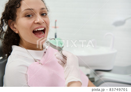Close-up of dentist hand removing dental impressions of the upper jaw made of silicone material of a woman patient sitting in dentists chair. Dental molds . Imprint of the tooth row of high precision. Close-up of dentist hand removing dental impressions of the upper jaw made of silicone material of a woman patient sitting in dentists chair. Dental molds . Imprint of the tooth row of high precision. 83749701
