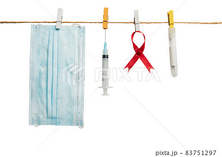 Red ribbon, syringe, and face mask hanging on the rope with white background 83751297