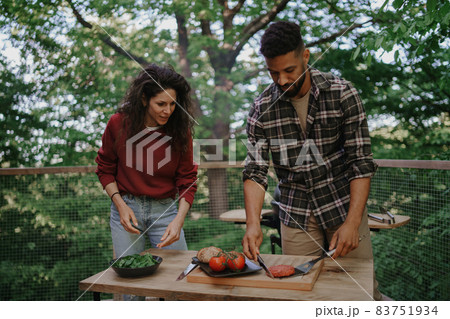 Happy biracial couple resting and preparing burgers outdoors in a tree house, weekend away 83751934